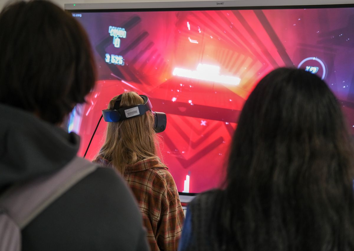 Besucherin spielt ein VR-Spiel, andere schauen am großen Bildschirm zu